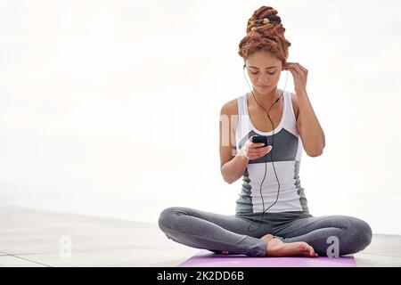 Die perfekte Begleitung zu ihrer Yoga-Session. Aufnahme einer jungen Frau, die Musik hört, während sie draußen Yoga praktiziert. Stockfoto