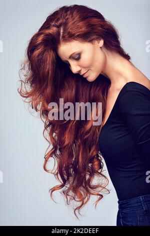 Los, lass deine Haare runter. Studioaufnahme einer jungen Frau mit schönen roten Haaren, die vor einem grauen Hintergrund posiert. Stockfoto