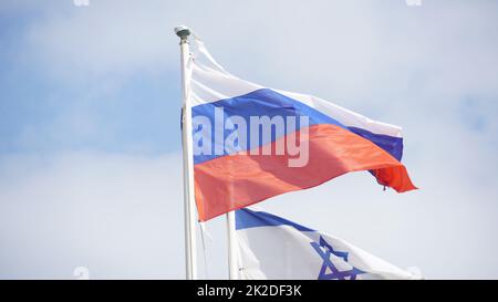 Russische und israelische Flaggen weben im Wind gegen den hellen Himmel Stockfoto