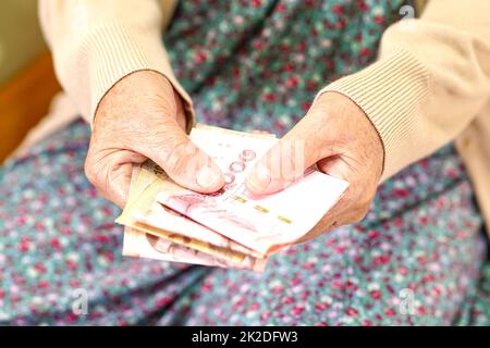 Ältere Patientin aus Asien, die Geldscheine in der Hand hält, Lebenshaltungskosten und medizinische Versorgung. Stockfoto