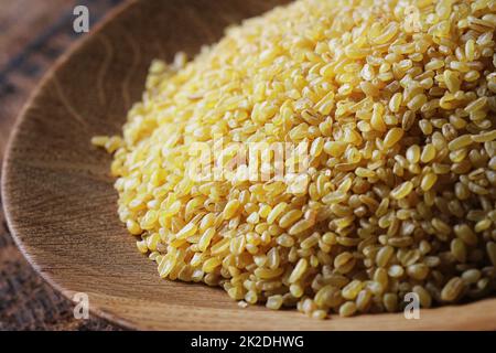 Trockener Bulgurweizen in Holzschüssel isoliert verschüttete Bulgur Stockfoto