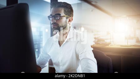 Konzentriert sich darauf, die Arbeit zu erledigen. Eine kurze Aufnahme eines hübschen jungen Geschäftsmanns, der spät im Büro arbeitet. Stockfoto