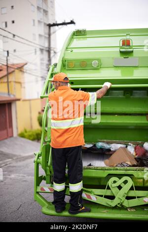 Weiter. Ein Müllsammler, der auf der Rückseite eines Müllwagens unterwegs ist. Stockfoto