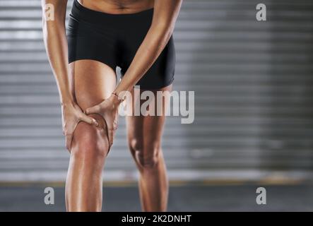 Sie blieb durch eine Verletzung in ihren Spuren stehen. Aufnahme einer Sportlerin mit Knieverletzung. Stockfoto