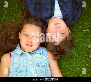 Halten Sie den Atem an. Hochwinkelige Aufnahme eines jungen Bruders und einer Schwester, die draußen auf dem Gras liegen und den Atem anhalten. Stockfoto