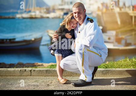 Papa und sein Liebling. Porträt eines Vaters in Marineinuniform, der mit seinem kleinen Mädchen auf dem Dock posiert. Stockfoto