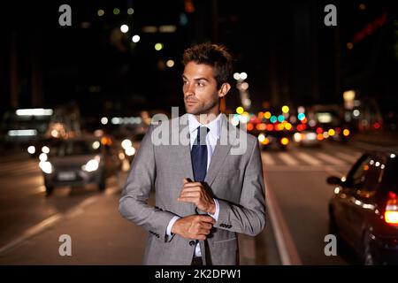 Suave in der Stadt. Ein gutaussehender Geschäftsmann, der nachts mitten in einer belebten Straße posiert. Stockfoto