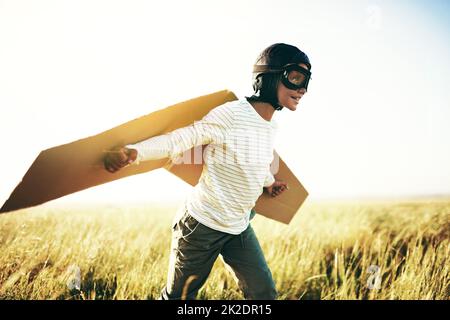 Bereit zum Abheben. Aufnahme eines Jungen, der vorgibt, mit einem Paar Pappflügeln auf einem offenen Feld zu fliegen. Stockfoto