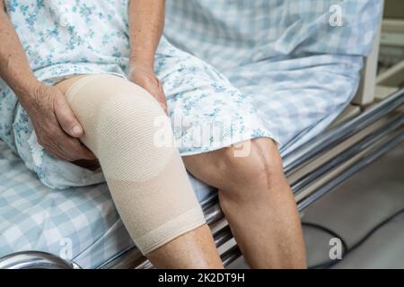 Asiatische ältere oder ältere alte Dame Frau Patientin mit Knieunterstützung Schmerzen Gelenk auf dem Bett in Krankenpflege-Station, gesund starke medizinische Konzept. Stockfoto