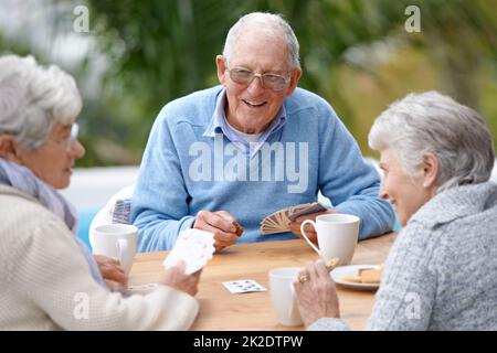 Ich kann diese beiden schlagen. Eine Gruppe älterer Bürger spielt zusammen Karten. Stockfoto