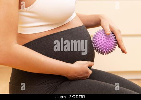 Eine Schwangerin massiert ihren Bauch mit einem stacheligen Gummiball Stockfoto