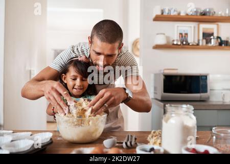 Backen bringt den Künstler in uns allen hervor. Kurzer Schuss eines jungen Mannes, der mit seiner kleinen Tochter zu Hause backt. Stockfoto