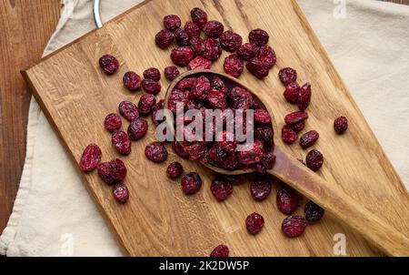 Ein paar getrocknete Preiselbeeren in einem Holzlöffel auf einem braunen Tisch. Köstliche Beeren, Blick von oben Stockfoto