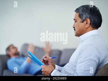 Reden ist die beste Therapie. Aufnahme eines Therapeuten, der sich Notizen gemacht hat, während er einem Patienten während einer Beratungssitzung zuhörte. Stockfoto