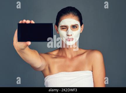 Die Leute auf meinem Blog werden das lieben. Studio-Sho einer jungen Frau, die ein Selfie beim Tragen einer Gesichtsmaske gemacht hat. Stockfoto