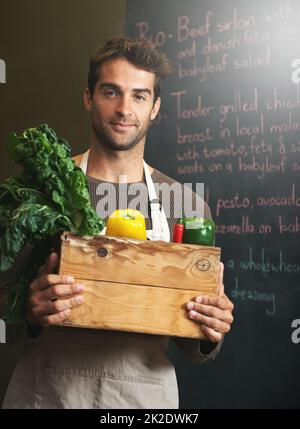 Er liebt sein Gemüse. Aufnahme eines jungen Mannes, der in seiner Küche eine Kiste mit frischem Gemüse in der Hand hält. Stockfoto