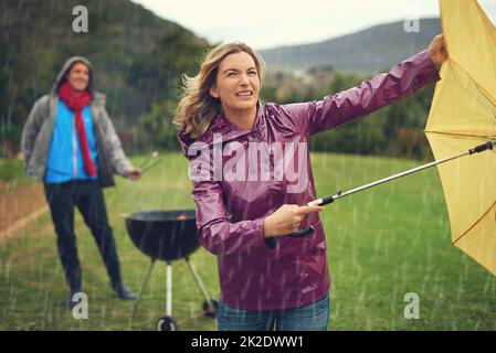 Wir werden uns nicht von einem schlechten Wetter abhalten lassen. Aufnahme eines Paares, das im Regen grillen wollte. Stockfoto