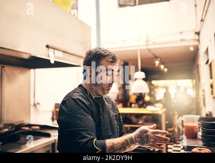 Er ist in seinem Element. Aufnahme eines fokussierten Küchenchefs, der in der Küche eines Restaurants ein Gericht zubereitet. Stockfoto