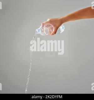 Gereinigtes Wasser. Zugeschnittenes Wasser, das vor grauem Hintergrund aus einer Flasche gegossen wurde. Stockfoto