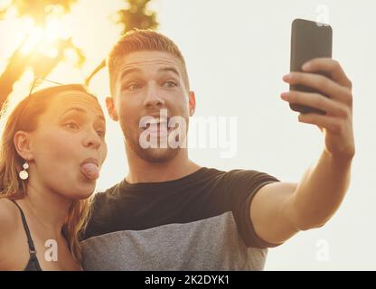 Setzen auf ihre albernen Selfie Gesichter. Aufnahme eines dummen jungen Paares, das draußen für ein Selfie posiert. Stockfoto