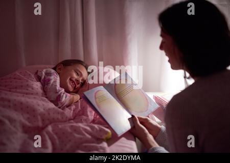 Geschichten, um ihre sweetdreams zu entfachen. Eine kurze Aufnahme eines kleinen Mädchens, das im Bett liegt, während ihre Mutter eine Schlafenszeit-Geschichte liest. Stockfoto