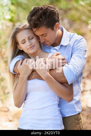Im Sonnenschein ihrer Liebe Beschnittene Ansicht eines jungen Paares, das sich mit geschlossenen Augen im Freien anhält. Stockfoto