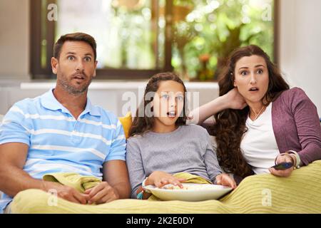 Absolut schockiert. Aufnahme einer Familie, die auf ihrem Sofa im Wohnzimmer sitzt und einen Film sieht und Popcorn isst. Stockfoto