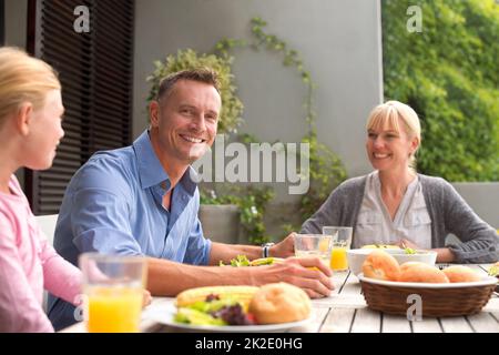 Genießen Sie das Mittagessen mit der Familie. Eine kurze Aufnahme einer glücklichen Familie, die an einem sonnigen Tag gemeinsam im Freien essen geht. Stockfoto