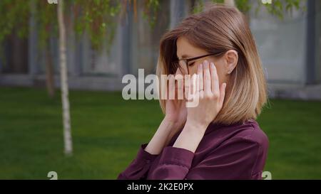 Porträt traurige junge Frau, die schlimme Kopfschmerzen hat, wenn sie draußen ihre Schläfe berührt. Stockfoto