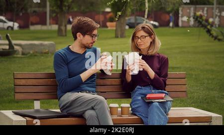 Hungriger junger Geschäftsmann genießt einen Snack. Essen Sie im Freien. Freunde, die einen Snack in einem Park zu sich nehmen. Freunde essen mit Gusto. Stockfoto