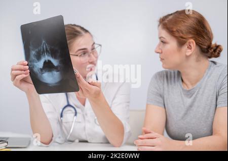 Eine Ärztin und ein Patient an der Rezeption diskutieren über eine Röntgenaufnahme der Nebenhöhlen. Stockfoto