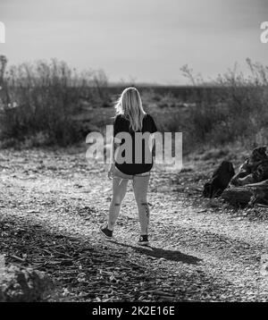 Rückansicht eines schönen blonden Mädchens mit langen Haaren, das bei Sonnenuntergang auf einem Feld läuft. Attraktive junge Frau genießt ihre Zeit draußen im Park. Travel pho Stockfoto