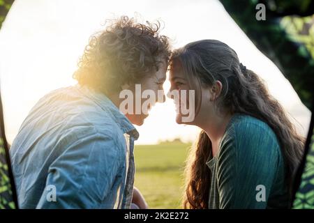 Angehende Romantik in der freien Natur. Aufnahme eines jungen Paares, das sich auf einem Campingausflug vor dem Zelt aufbondelt. Stockfoto