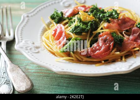 Köstliche würzige Linguine Pasta mit gebratenem Kohlkohl, Speck, Knoblauch und Parmesan auf einem weißen Teller Stockfoto