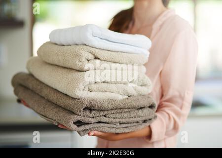 Frische Wäsche. Aufnahme einer jungen Frau, die einen Stapel gefalteter Handtücher trägt. Stockfoto