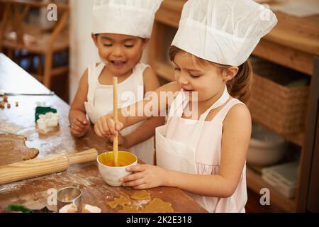 Backen macht so viel Spaß. Zwei kleine Mädchen haben Spaß beim Backen in der Küche. Stockfoto