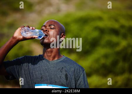 H2O - Ein bester Freund des Läufers. Aufnahme eines jungen männlichen Läufers, der während eines Rennens aus seiner Wasserflasche trinkt. Stockfoto