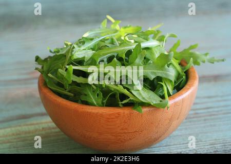 Frische Rucolablätter in einer Holzschüssel, Rucola auf altem Holzhintergrund Stockfoto