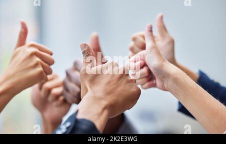 Wir lieben das, was Sie tun. Aufnahme einer Gruppe von Mitarbeitern, deren Arme in der Geste mit den Daumen nach oben angehoben wurden. Stockfoto