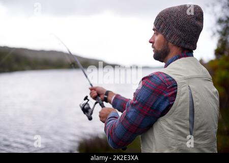 Warten auf den Fisch zu beißen. Aufnahme eines hübschen Mannes, der an einem natürlichen See angeln soll. Stockfoto