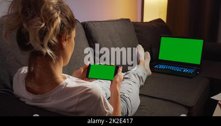 Frau, die auf einem Sofa mit Telefon und Laptop mit grünem Bildschirm liegt Stockfoto