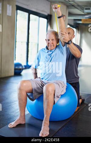 Dehnung und Kräftigung. Ein Trainer hilft einem älteren Mann mit Fitness. Stockfoto