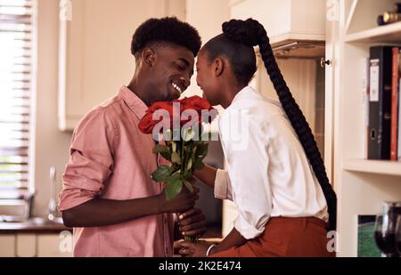 Schöne Blumen für meine schöne Dame. Kurzer Schuss eines anhänglichen jungen Mannes, der seiner Frau zu Hause in ihrer Küche einen Strauß Rosen gab. Stockfoto