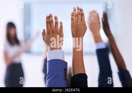 Sie haben alle Antworten. Aufnahme einer Gruppe von Menschen, die in einer Klasse die Hände heben. Stockfoto