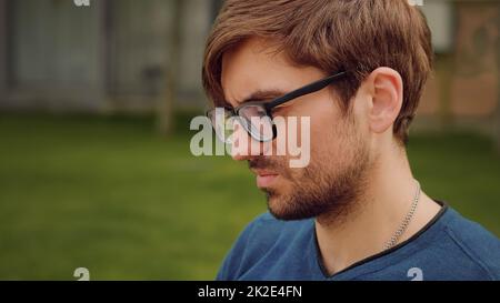 Ein Mann arbeitet an seinem Laptop, während er draußen auf einer Bank sitzt. Fokussierte Gesichtsausdrücke. Konzentrations-Gesichtsportrait. Verantwortungsvolles Arbeiten. Ein hübscher junger Mann schreibt eine seriöse Post. Stockfoto