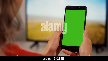 Vertikaler grüner Bildschirm für Copy Space Chroma Key Mockup-Markierungen und Alpha-Matte. Rückansicht über die Schulter Mädchen sieht sich die Nahaufnahme auf dem Bildschirm an. Stockfoto