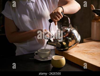 Brühen der perfekten Tasse. Eine kleine Aufnahme einer jungen Frau, die in ihrer Küche eine Tasse Tee zubereitet. Stockfoto