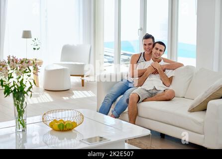 Unser Haus ist voller Liebe. Porträt eines jungen schwulen Paares, das sich zu Hause auf einem Sofa entspannt. Stockfoto