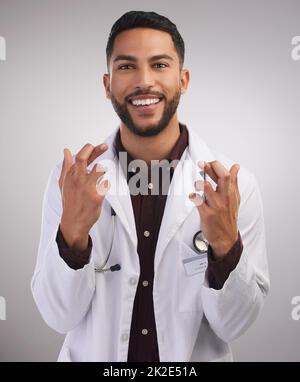 Nun, Finger und Zehen sind gekreuzt. Aufnahme eines hübschen jungen Arztes, der allein im Studio mit gekreuzten Daumen für Viel Glück. steht Stockfoto