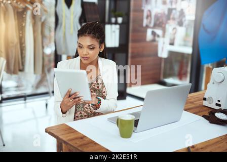 Design im Handumdrehen. Eine kurze Aufnahme einer jungen Modedesignerin, die an ihrem Tablet arbeitet. Stockfoto